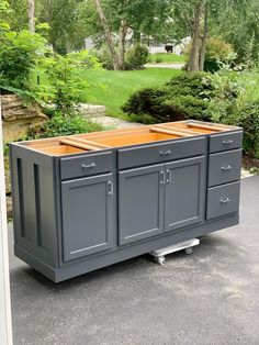 a kitchen island with two doors and drawers on the top, in front of some trees