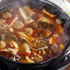 a pot filled with meat and vegetables cooking on top of a stove burner next to a wooden table