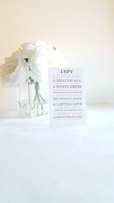 a white flower in a glass vase with a card saying i spy on the side