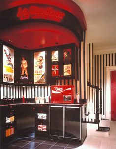 a room with black and white stripes on the walls, red neon signs above the bar