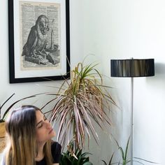 a woman sitting in front of a potted plant next to a wall mounted print