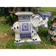 an elephant statue sitting on top of a lush green field next to two vases