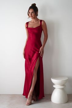 This gown is your perfect choice for debs, prom or any formal event. A look that blends classic glamour with contemporary style. Designed for timeless allure and effortless sophistication. Featuring a graceful cowl neckline and thick shoulder straps, this dress offers a flattering, structured fit. The sultry thigh-high slit adds a bold, modern touch, while the luxurious satin fabric drapes beautifully to enhance your silhouette. Highlights Stunning red gown with cowl neckline Soft satin material Satin Evening Dress With Lace-up Back, Satin Gown With Lace-up Back And Fitted Bodice, Red Satin Bridesmaid Gown, Fitted Satin Gown With Lace-up Back, Satin Gown With Ruched Back, Satin Maxi Dress With Lace-up Back For Prom, Satin Gown With Corset Back And Maxi Length, Satin Evening Dress With Lace-up Back And Fitted Bodice, Satin Gown With Ruched Back For Gala