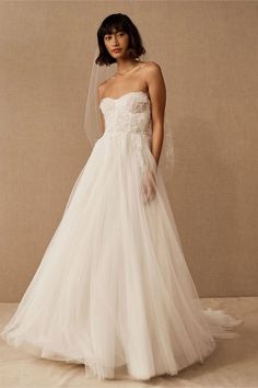 a woman in a white wedding dress with a veil on her head, standing against a beige background