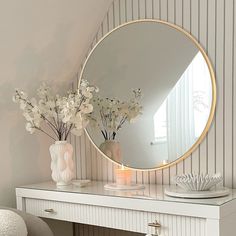 a white desk with a round mirror and flowers on the top shelf in front of it