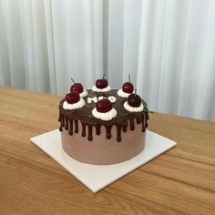 a chocolate cake topped with cherries and drizzled in icing on top of a wooden table