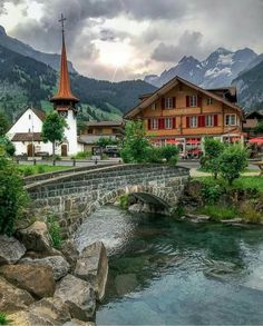 a river running through a lush green hillside next to a wooden building with a steeple in the background