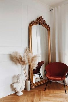 a mirror sitting on top of a wooden floor next to a red chair and vase