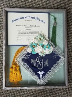 an embroidered graduation cap with flowers and tassels in a shadow box on the floor