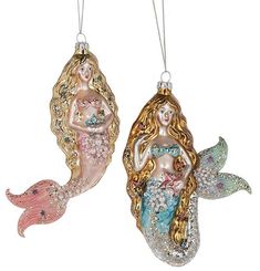 two christmas ornaments with mermaids hanging from strings on a white background, one in gold and the other in pink