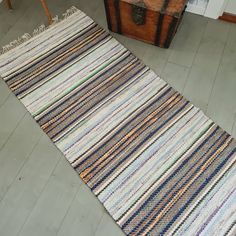 a multicolored striped rug on the floor next to a chest of drawers and an old trunk