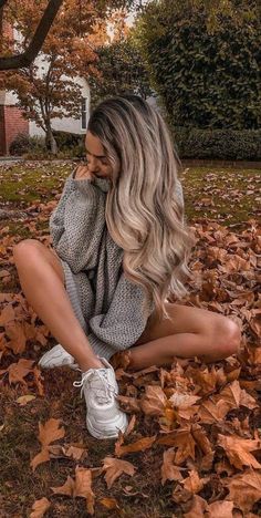 a woman sitting on leaves talking on her cell phone in the middle of an autumn day