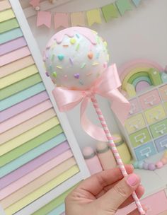 a hand holding a pink lollipop with sprinkles and a ribbon