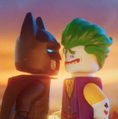 the lego batman movie character is standing next to another person in front of a sunset