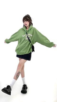 a woman in a green sweatshirt and black skirt is posing for the camera with her arms spread out