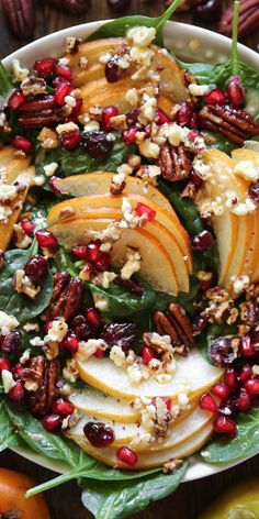 a white bowl filled with apples, spinach and cranberry sauce on top of a wooden table