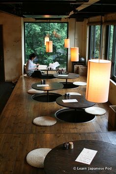 a person sitting at a table in a room with lots of round tables and lamps