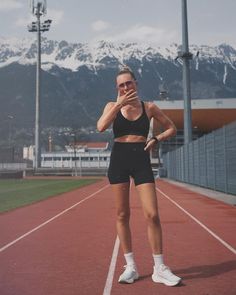 a woman standing on a track with her hand to her mouth and wearing black shorts