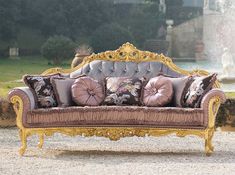 an ornate couch sitting in the middle of a gravel road next to a stone wall