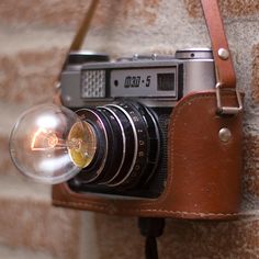 an old fashioned camera hanging on a brick wall with a light bulb in it's holder