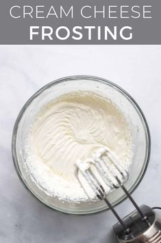 a whisk in a glass bowl with cream cheese frosting next to it