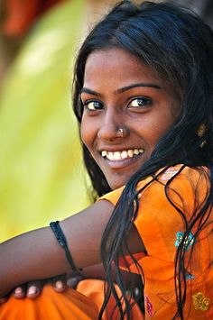 a woman in an orange dress smiling at the camera with her hand on her hip