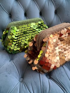 two sequin bags sitting on top of a blue velvet couch next to each other