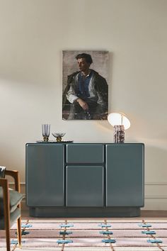 a living room with a painting on the wall next to a blue cabinet and two chairs