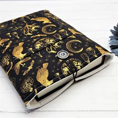 a black and gold cloth covered book sitting on top of a white wooden table next to a blue flower