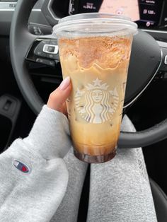 a person holding up a starbucks drink in their hand with the steering wheel behind them