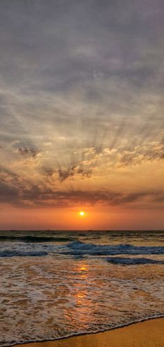 the sun is setting over the ocean with waves lapping in front of it,