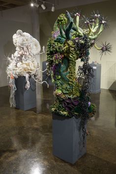 two sculptures made out of flowers and plants on pedestals in an art museum setting