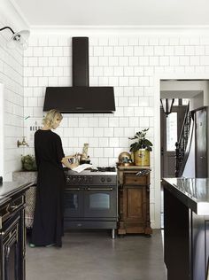 a woman standing in a kitchen with an oven and range hood over her head on the counter