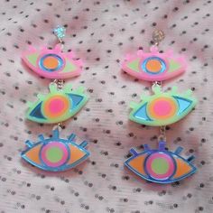 three colorful earrings are hanging on a white fabric surface with dots and circles in the center