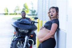 a pregnant woman leaning against a wall next to a motorcycle with a man in the background