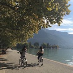 two people riding bikes on the side of a lake