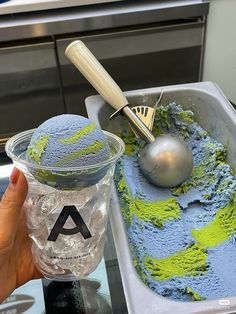 a person holding up a cup filled with blue and green ice cream next to a spoon