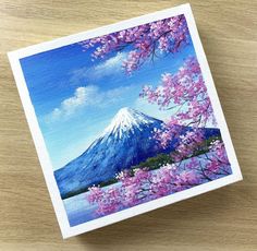 a painting of a cherry blossom tree with a mountain in the background on a wooden surface