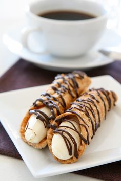 two desserts with chocolate drizzled on them sitting on a plate next to a cup of coffee