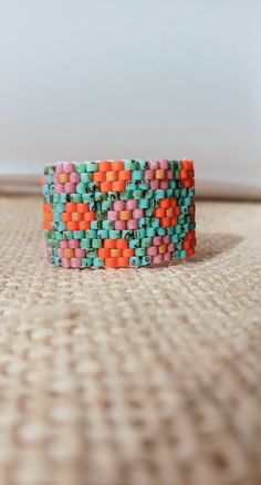 an orange, green and pink beaded bracelet sitting on top of a carpeted floor