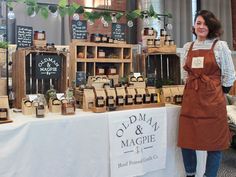 a woman standing in front of a table with jars and bottles on it at an outdoor market