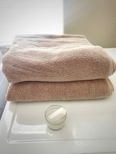 two towels folded on top of each other next to a small jar of white liquid