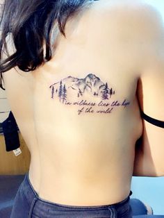 the back of a woman's shoulder with trees and mountains tattoo on her left side