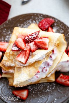 pancakes with strawberries and powdered sugar are on a plate, ready to be eaten