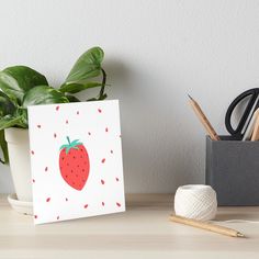 a card with a strawberry on it sitting next to a potted plant art board print