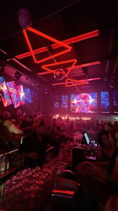 a group of people sitting at a bar with neon lights on the ceiling and laptops in front of them