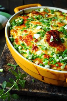 mexican casserole with green onions and cheese in a yellow dish on a wooden table