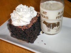 a piece of chocolate cake with whipped cream on top next to a glass of milk