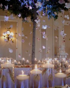 a room filled with lots of tables covered in white table cloths and lit candles