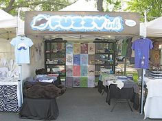 an outdoor market with clothes and t - shirts for sale on the tables in front of it